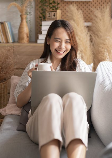 young attractive asian female working at home hand use laptop checking search schedule working process planning report with leisure relax on sofa in living room with morning light peaceful moment